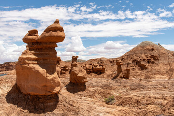 Mushroomlike sandstone rock formations called goblins and eroded cliffs in Goblin Valley State Park, Utah, USA against a white clouded blue sky