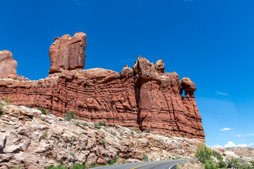 Drivers perspective over the road approaching the Three Penguins rock formation against a blue sky in Arches National Park, Moab, UT, USA