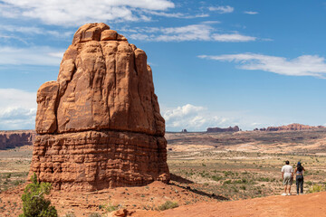 Man and woman overlooking the sandstone formations seen from La Sal Mountains Viewpoint in Arches National Park, Utah, USA with balanced rock in far distance