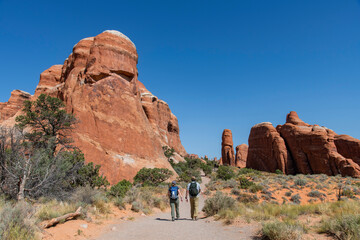 Two people walking along Devil's Garden Trail in Devil’s Garden district in Arches National Park, Utah, USA towards geological sandstone formation Tunnel Arch with, tunnel-like hole in the middle