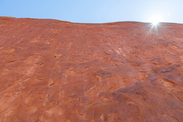 Low angle view of steep vertical geological sandstone formation with bright sun and sun rays along Devils Garden Trail in Devil’s Garden district in Arches National Park, Utah, USA