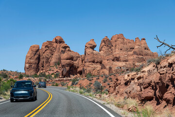 Drivers perspective over the Arches Scenic Drive road with cars approaching landmark geological sandstone formation of Broken Arch against a blue sky in Arches National Park, Moab, UT, USA