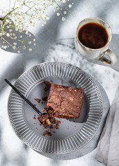 Chocolate brownie with nuts on a dark plate on a light background with cup of coffee