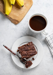 Vegetarian chocolate banana brownie on a plate on a light background with a cup of coffee