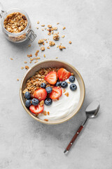 Natural greek yogurt with granola, blueberry and strawberry in a bowl on a light background