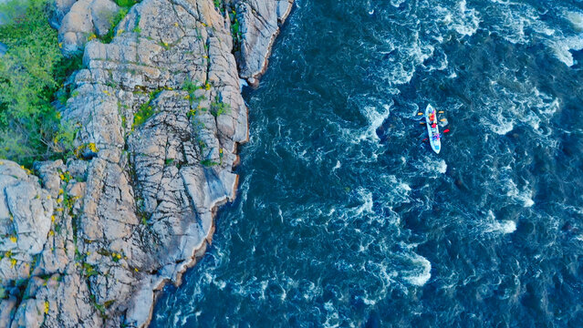 Aerial view of a kayak floating on a turbulent river between forest and stone cliffs.