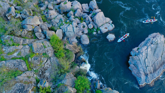 Aerial view of two kayaks navigating through a narrow rocky river pass surrounded by large boulders and lush vegetation in a scenic natural landscape.