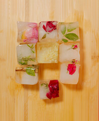 Creative arrangement of colorful flowers in ice cubes on wooden background. Sunny day concept.