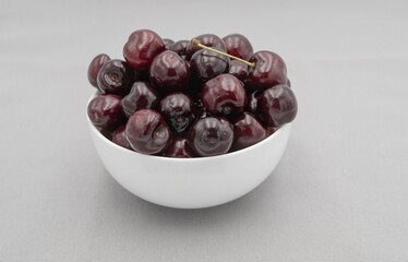 Fresh dark cherries in ceramic bowl on neutral gray cloth – minimal food photography