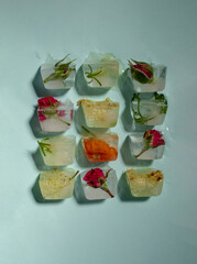 Creative arrangement of colorful flowers in ice cubes on blue background. Sunny day concept.