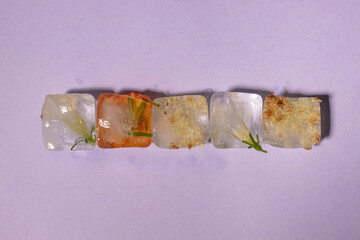 Creative arrangement of colorful flowers in row in ice cubes on pastel purple background. Sunny day concept.