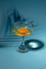 Raw egg in the glass on pastel blue background. Sunny day concept.