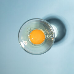Raw egg in the glass on pastel blue background. Sunny day concept. Flat lay