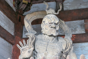 Ancient wooden statue of a Nio guardian, Agyō, is captured with a ferocious expression and open mouth. Powerful and symbolic protector at the entrance of a traditional Buddhist temple in Kyoto, Japan.