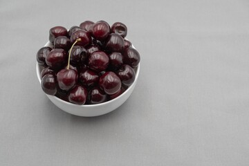 Fresh dark cherries in ceramic bowl on neutral gray cloth – minimal food photography