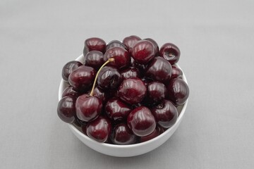 Fresh dark cherries in ceramic bowl on neutral gray cloth – minimal food photography
