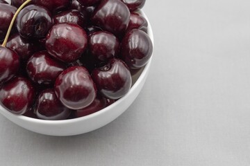 Fresh dark cherries in ceramic bowl on neutral gray cloth – minimal food photography