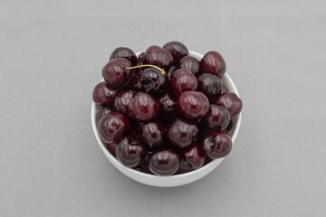 Fresh dark cherries in ceramic bowl on neutral gray cloth – minimal food photography