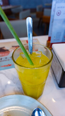 Iced orange juice in a glass with a straw made from lemongrass stalks on a dining table in a restaurant