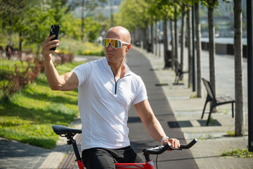 Fototapeta premium Caucasian cyclist taking selfie on smart phone in park. Outdoor activity.