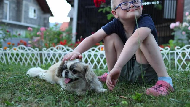 Cute boy with Down syndrome petting a small dog in the yard. Home, authentic, candid family moments, love, joy.