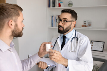 Male Latin physician doctor in glasses and lab coat prescribing medication to patient, giving...
