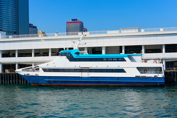 A large ferry is docked at a waterfront terminal under clear blue skies. The vessel is blue and...