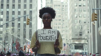 Woman in city holds powerful sign expressing strength and confidence - Powered by Adobe