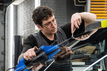 Automobile special workers replacing windscreen or windshield of a car in auto service station...