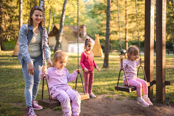Mother is rocking her twin daughters on a swing in the park