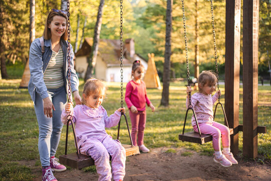 Mother is rocking her twin daughters on a swing in the park - Powered by Adobe