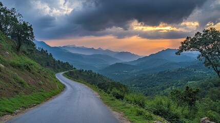 A paved road runs through green mountains under a cloudy sunset sky. A scenic outdoor road view.
