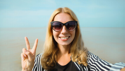 Happy cheerful young woman smiling taking selfie with smartphone on the beach, joyful girl on sea