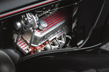 A detailed shot captures the powerful engine of a classic black hot rod car with chrome accents.