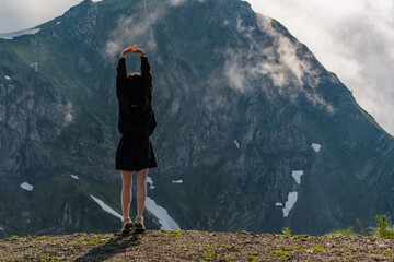 Rear view of a young woman standing on the edge of a slope in the mountains in summer.