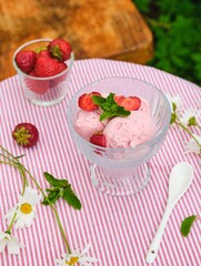Three scoops of creamy strawberry ice cream with fresh strawberries in a glass bowl on a table with a tablecloth in the yard. Summer desserts.