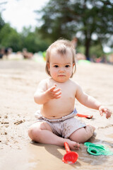 cute baby with sand toys enjoying a sunny day at the beach surrounded by trees and sunlight in a...