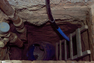 Shallow excavation features wooden ladder, drainage pipes, and a blue barrel at the bottom, indicating ongoing construction work