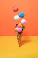 Multicolored ice cream scoops in ice cream cone on yellow and orange background. Vibrant colors