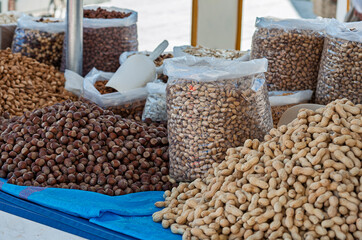 A vibrant display of assorted nuts and dried fruits, including hazelnuts and peanuts, on an outdoor...