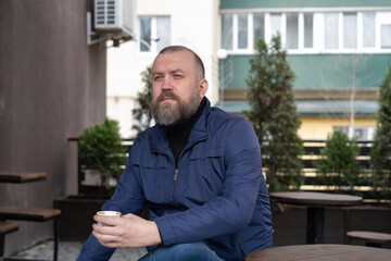Man enjoying coffee outside a cafe during daytime in a modern urban setting with trees around