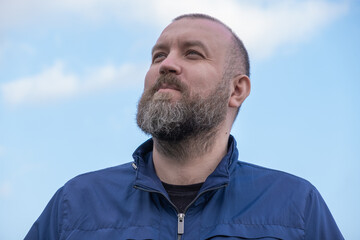 Man with beard looking up at a clear sky during a sunny day outdoors in a relaxed posture