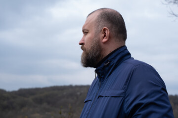 Man contemplatively gazes into the distance while standing outdoors in a rural landscape under...