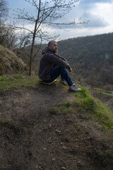 Man rests on a hillside overlooking a serene valley during a cloudy afternoon