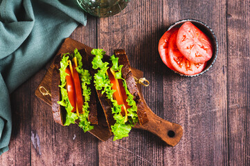 Vegetarian sandwich with tomato, cheese and lettuce on a board on a table top view