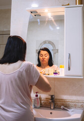Woman doing her morning rituals standing against the mirror in the bathroom