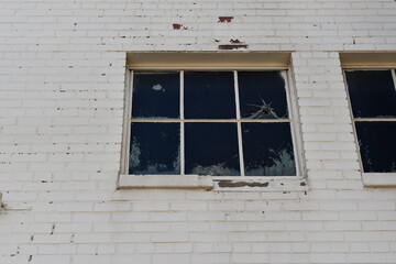 Window on side of brick building. White chipping paint. Cracked panes.