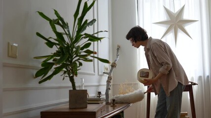 Focused neat young woman wiping dust with duster at home on furniture carefully lifting items. Household cleaning, indoor maintenance, organized approach, daily chores, domestic routine, tidy space