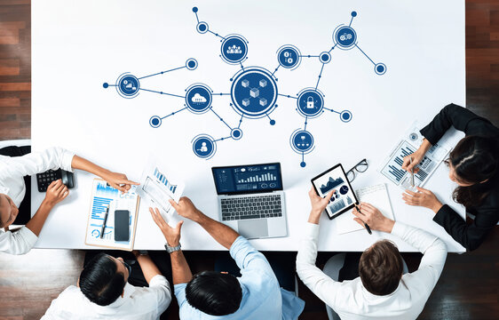 A vibrant business meeting showcasing technology and data visualization on a sleek table. Professionals engage with laptops and tablets, sharing insights and strategies in a modern workspace. Amity