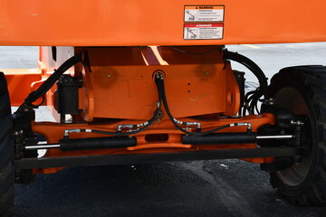 High lift machine front steering control mechanisms. Bright orange personnel lifter. Hazard stickers on counterweight.